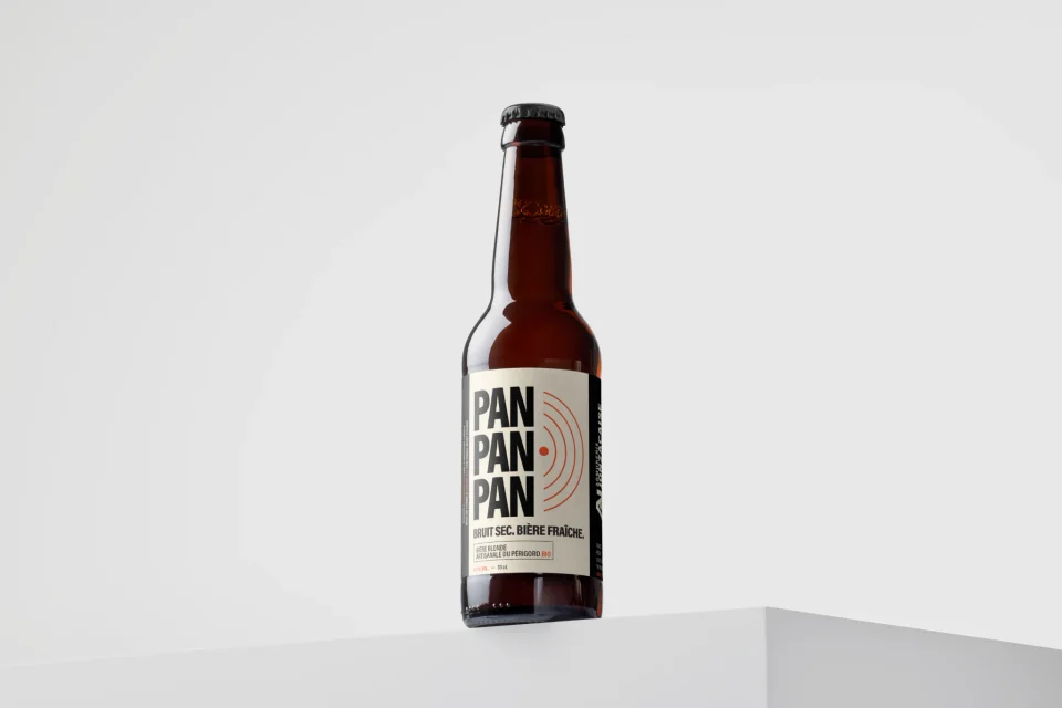 Mockup d’une bouteille PAN PAN PAN isolée sur un socle blanc, présentant l’étiquette typographique noire et les ondes rouges.