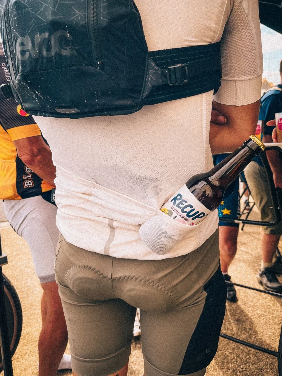 Photographie d’un cycliste vu de dos portant une bouteille de bière RÉCUP’ dans la poche arrière de son maillot.